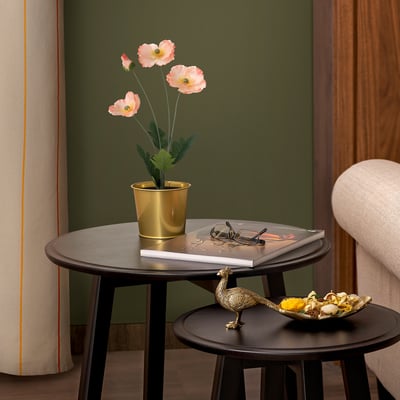 Stylish, dark tables holding golden pot with pink flowers, books, and bowl. Indoor decor.