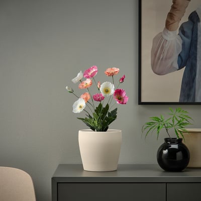 Small white artificial FEJKA plant sits on a dark console, brightening a modern space.