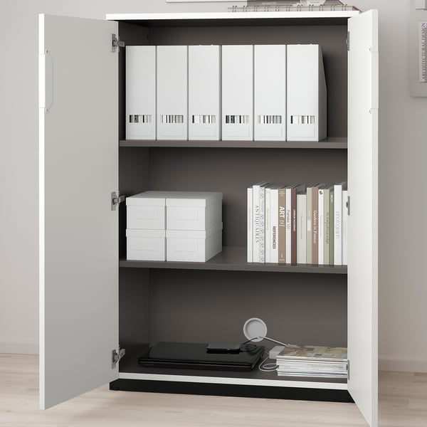 Open white cabinet with adjustable shelves holding white binders, books, and black folders. Shelves organised for office storage, with cords behind.