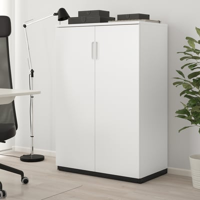 White GALANT cabinet on wood floor, tall & modern with double doors, next to black chair & desk.