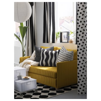 Modern living room with yellow sofa, black and white patterned curtains, pillows, and rug. Large windows let in natural light.