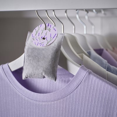 A closet with white hangers holding purple clothing and a lavender-scented bag.
