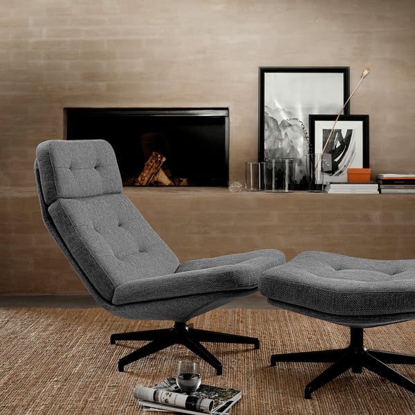 Modern grey fabric swivel chair and ottoman, wooden floor, rug, fireplace, framed art, glass, books.
