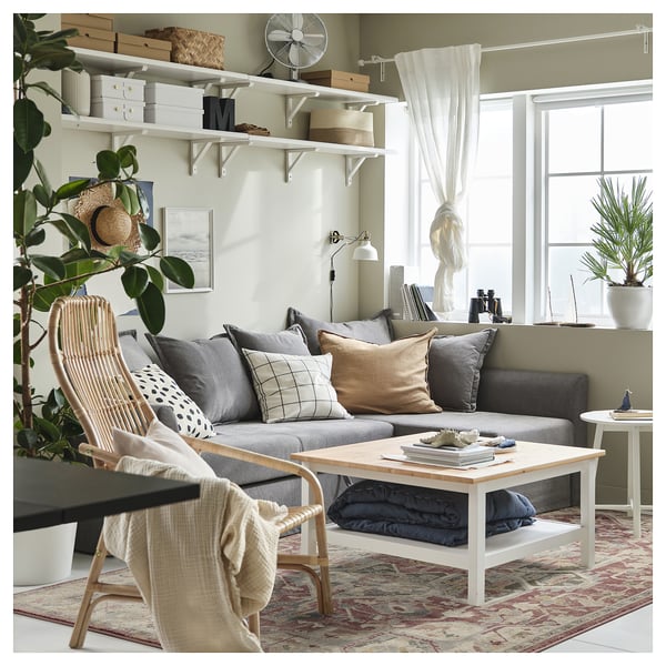 Bright living room with grey couch, patterned rug, white coffee table, wooden chair, and potted plants.
