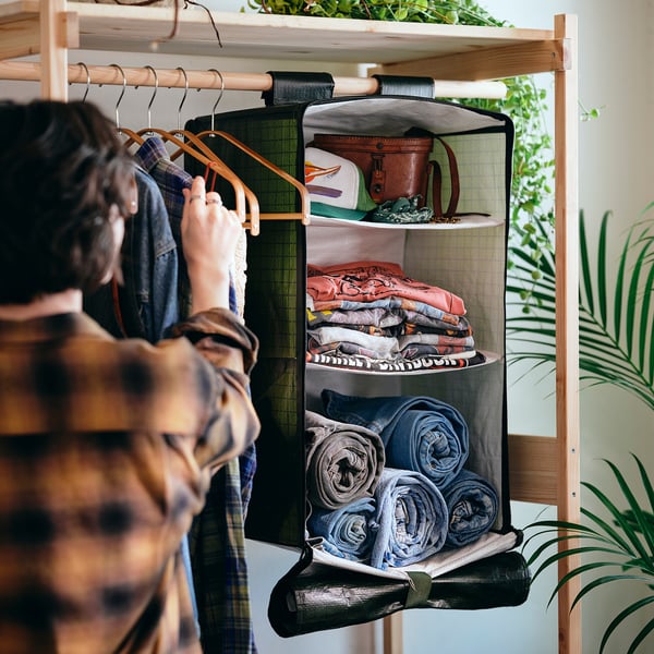 Person organising clothes in wooden wardrobe, KOMPISHÄNG bag with folded clothes and towels.