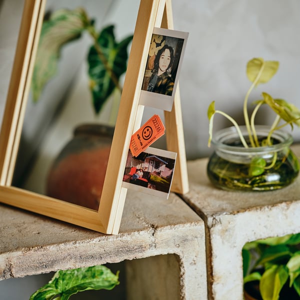 Wooden photo display stand with polaroid pictures, notes, and plant on textured shelf.