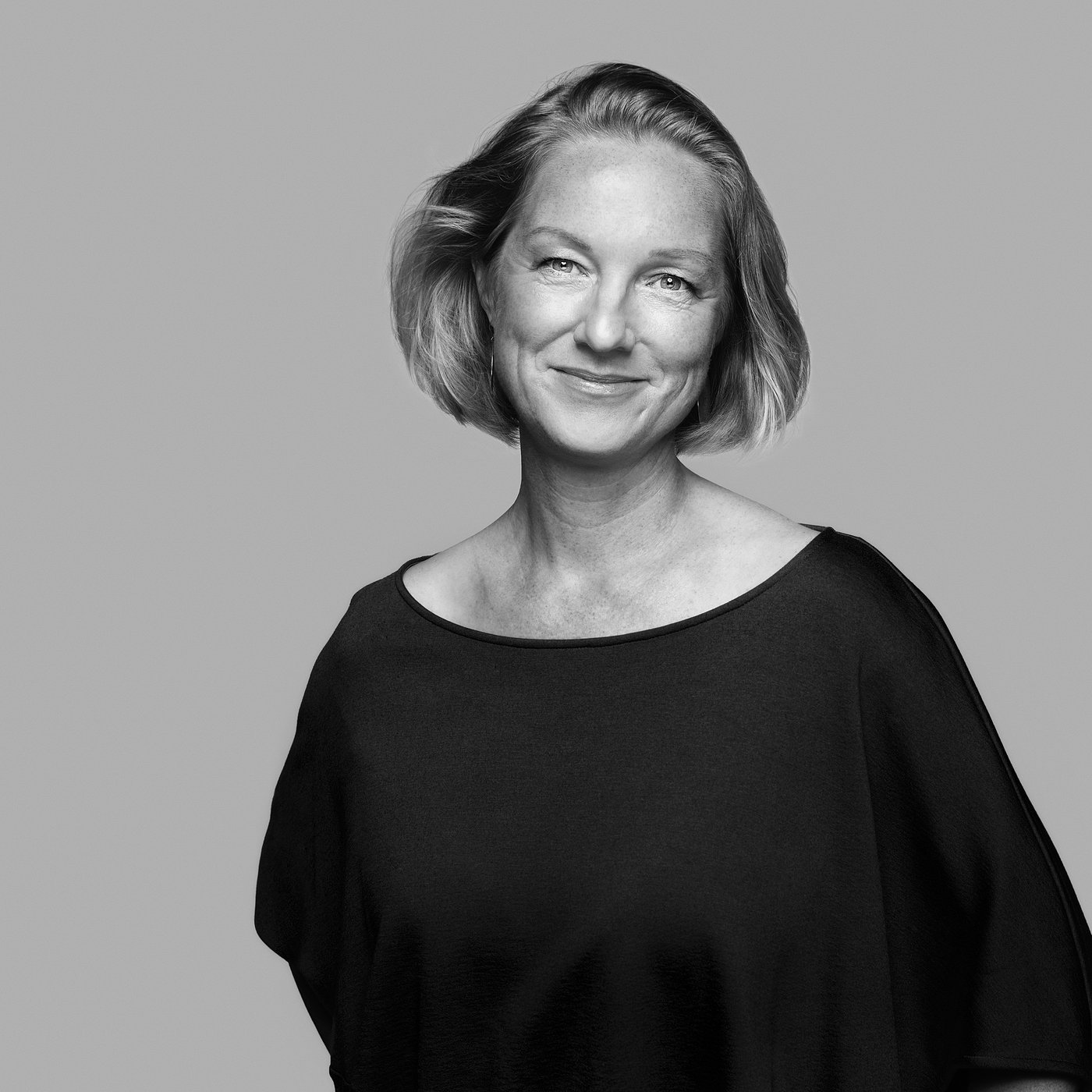 Black and white portrait of the designer with short hair in a dark top, smiling confidently.