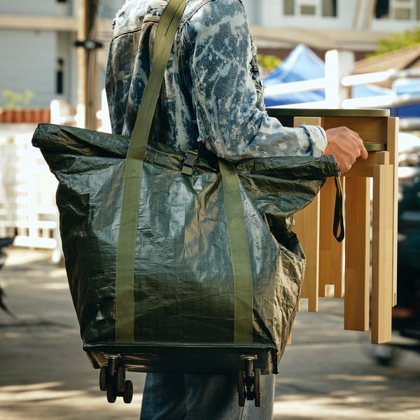 Person pulls large, wheeled shopping bag on street. The bag has a foldable top for secure closure. Easy to manoeuvre with long straps.