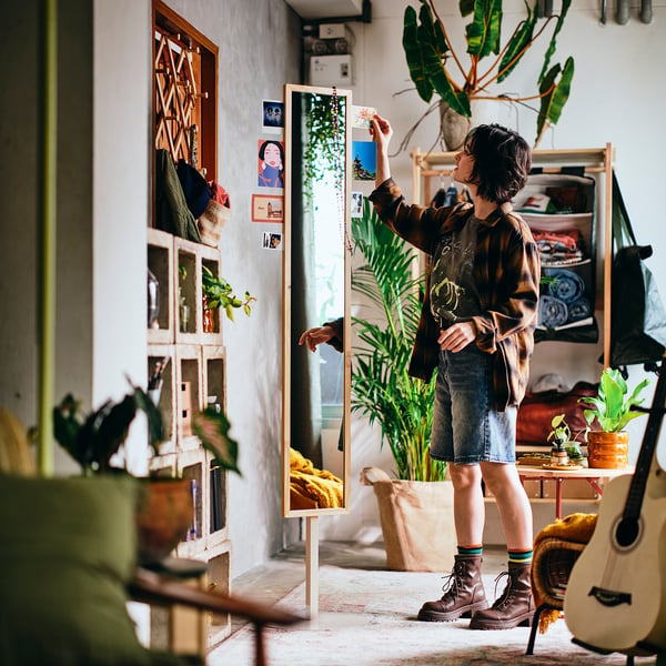Person adjusting mirror with hooks and photo slots in boho room.
