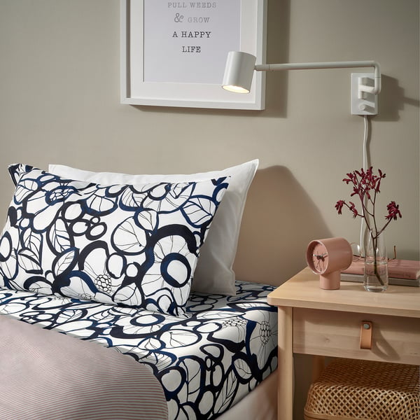 Blue-black floral bedding in bedroom with pillows, peach clock, flowers, wall light.