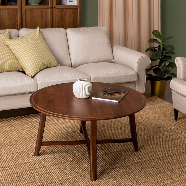 Round wooden coffee table with vase and magazine, placed in front of a beige sofa with striped pillows.