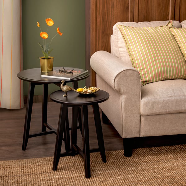 Cosy living room with beige sofa, nesting tables, and striped pillow. Tables hold decor and plant.