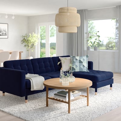 A modern living room with blue LANDSKRONA sofa, woven pendant light, wooden coffee table, and large windows offering a serene outdoor view.