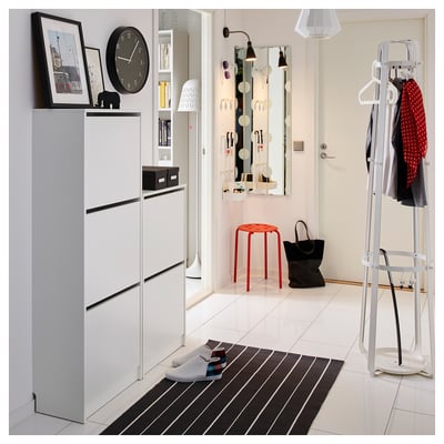 Modern entryway with white floor, black and white striped rug, shoe rack, clock, mirror, coat rack, red stool, and black bag.