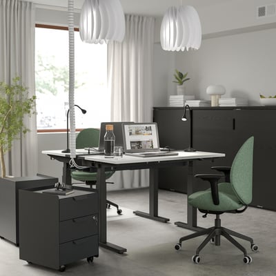 Minimalist office with 2 MITTZON desks, green chairs, pendant lamps, standing heights, computers, large windows.