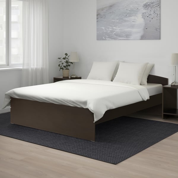 NODELAND bed: sleek, dark brown, rounded, large, wood-like floor, fits standard mattresses, white linens, black rug, light-filled, minimalist design.