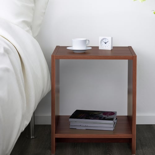 Bedside table with open shelves, holding a coffee cup, clock, and stack of magazines.