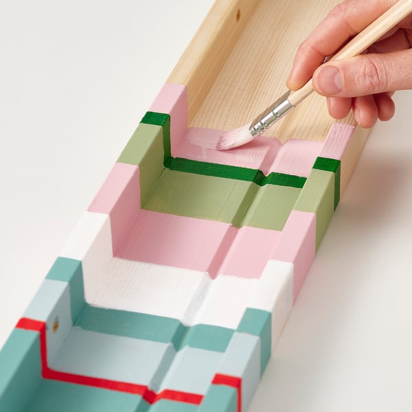 Hand paints a colourful wooden step display shelf, ideal for showcasing photos and art.