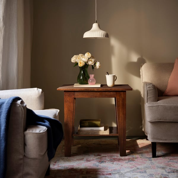 NORRVÅGA side table with mango wood. Flowers, books, pink vase, and mug on top. Pendant light nearby.