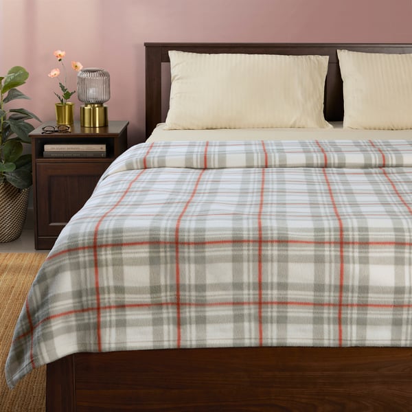 Plaid blanket on bed with pillows, side table, lamp, books.