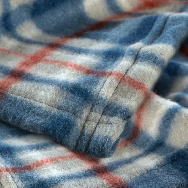 Close-up of soft, recycled fabric blanket with blue, white, and red checks, showing its cosy, high-quality texture.