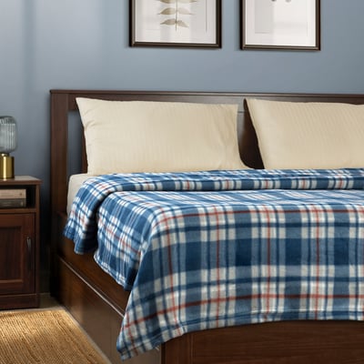 Blue & white chequered blanket on bed, made of recycled polyester. Two white pillows, bedside table with lamp, and two framed wall pictures.