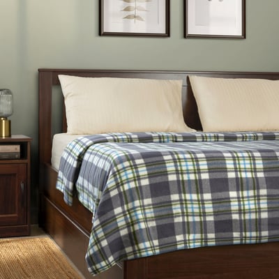 ODENSLÄTA blanket on bed, blue-green-white chequered, soft, with pillows & lamp.