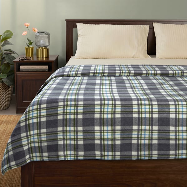 A blue-green plaid blanket on a bed with pillows and a plant. Made of recycled polyester, it almost covers the entire bed.