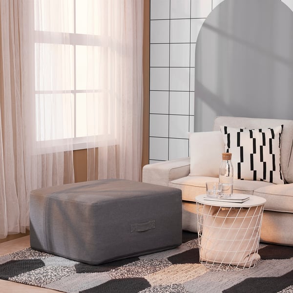 Modern living room with beige sofa, grey pouffe, and wire side table. Sheer curtains by large window.