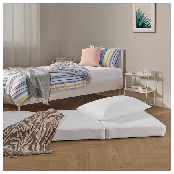 ÖVERBORG pouffe as guest bed in cosy room. White, recycled polyester, fits under twin bed. Stripes & neat table.