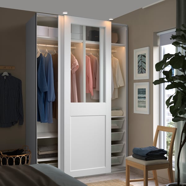 Modern bedroom with large PAX wardrobe, sliding glass doors exposing clothes, sleek white design.