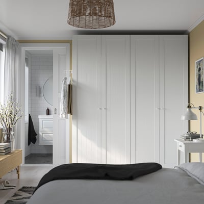 Modern bedroom large white PAX wardrobe against wall, tall and spacious, matching bed with grey blanket. Adjacent bathroom visible with white tiles.