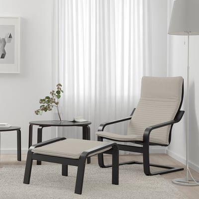 Modern living room with black POÄNG chair, beige footstool, side table vase, floor lamp, and large curtains.
