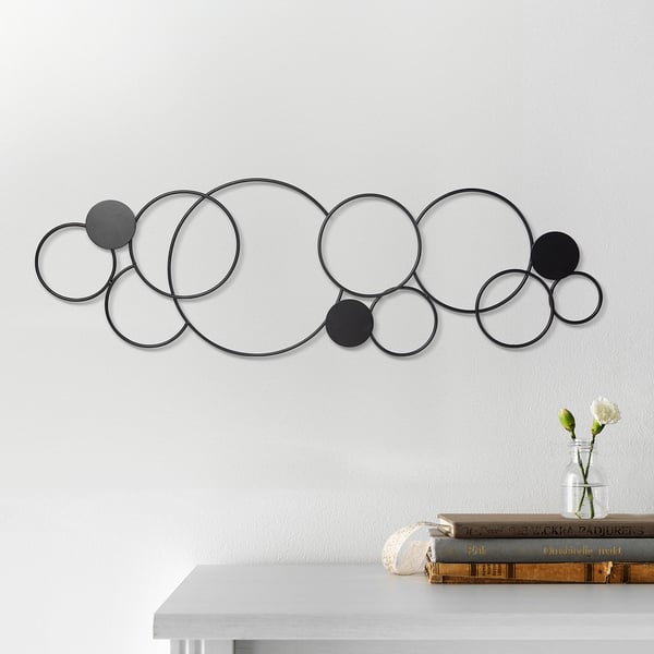 Modern black circular metal wall art hanging above a table with books and a vase of white flowers.