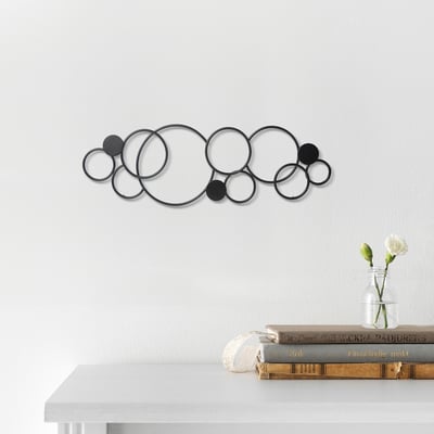 Abstract metallic wall sculpture with circles and dots, displayed above a shelf with books and a vase.