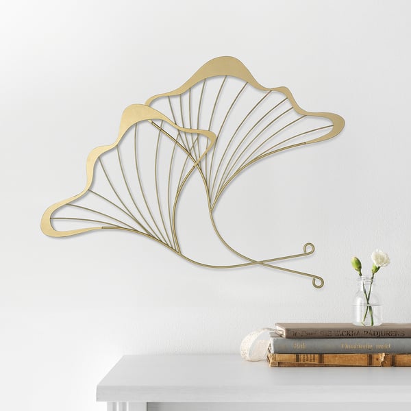 Gold decorative wall art, shaped like ginkgo leaves, hanging above a shelf with books and a vase of flowers.