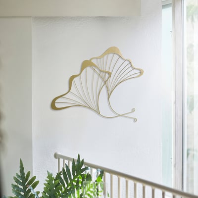 Gold-colored SILVERNÄBB wall decoration, made of steel, shaped like fanned leaves. Its larger than the nearby plant but smaller than the door.