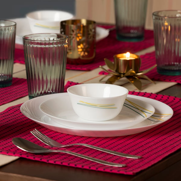 Elegant table setting: white bowl, red mat, pink napkin, candle, silverware, glass reflections.