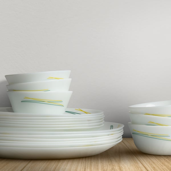 Stacked white opal glass dinnerware, featuring subtle yellow and blue lines, displayed neatly on a wooden surface.