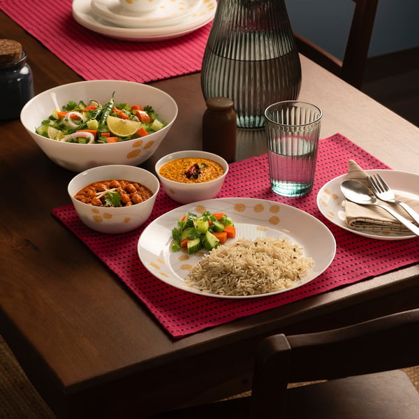 Dining table with yellow floral porcelain dishes, salad, curry, rice, vegetables, cutlery, and decorative glass.