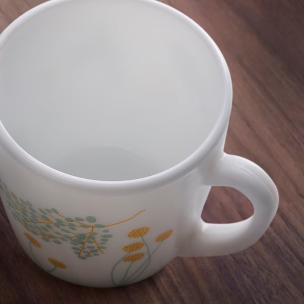 White mug with green and yellow floral pattern, glossy finish, sitting on a wooden table.