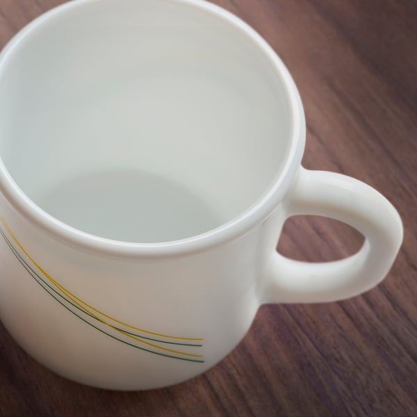 Empty white mug with yellow lines on wooden table. High-quality, glossy finish, easy to hold handle.