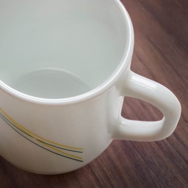 Empty white mug on wooden table, showcasing sleek handle and elegant line design.
