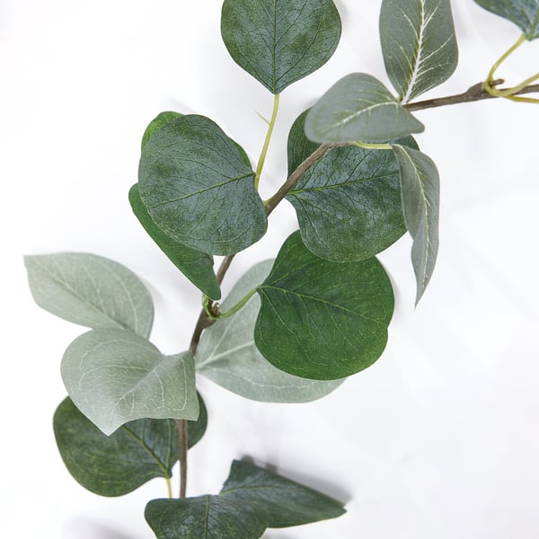 Large green leaves of artificial garland, vivid and lifelike, arranged on a branch.