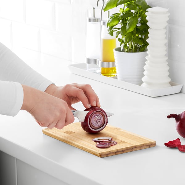 Person slicing red onion on a bamboo cutting board on a white countertop.
