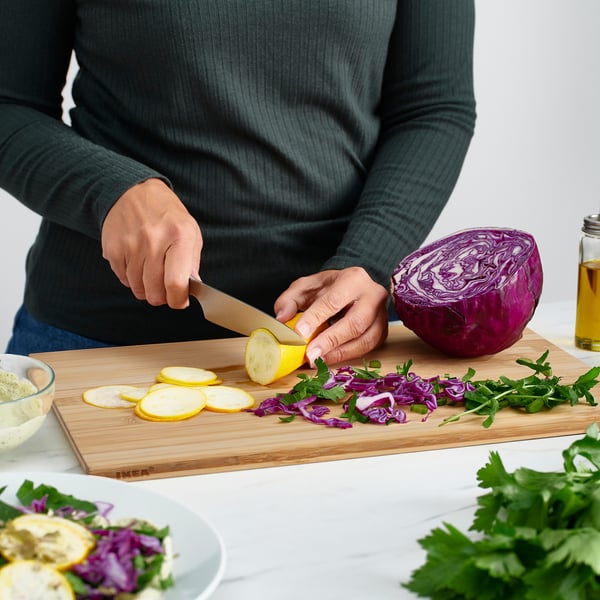 A person slices lemons on a bamboo cutting board. The chopping board has slanted edges for easy grip.