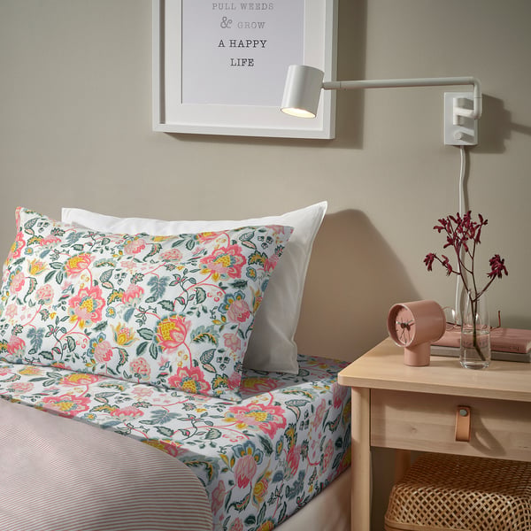 Floral bed, pink alarm, wall light, books, flowers.