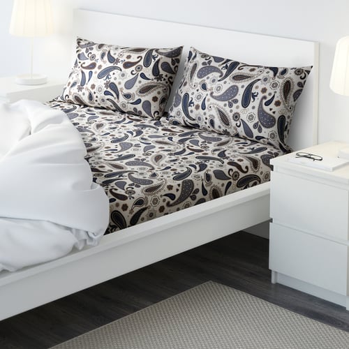 Cosy bed with paisley-patterned SÖTBLOMSTER cotton duvet cover and pillowcases, white bed frame, bedside table, and lamp.