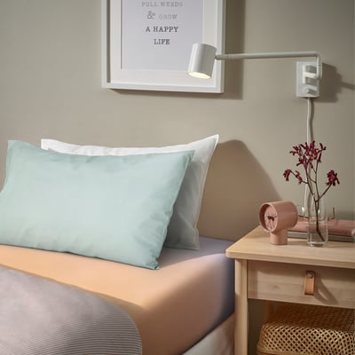 Bedroom with pale blue bedding, wall art, lamp, clock, flowers, and basket.