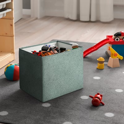 Large STJÄRNSKOTT green dotty box stores toys, fits well near shelves, handy for playroom.